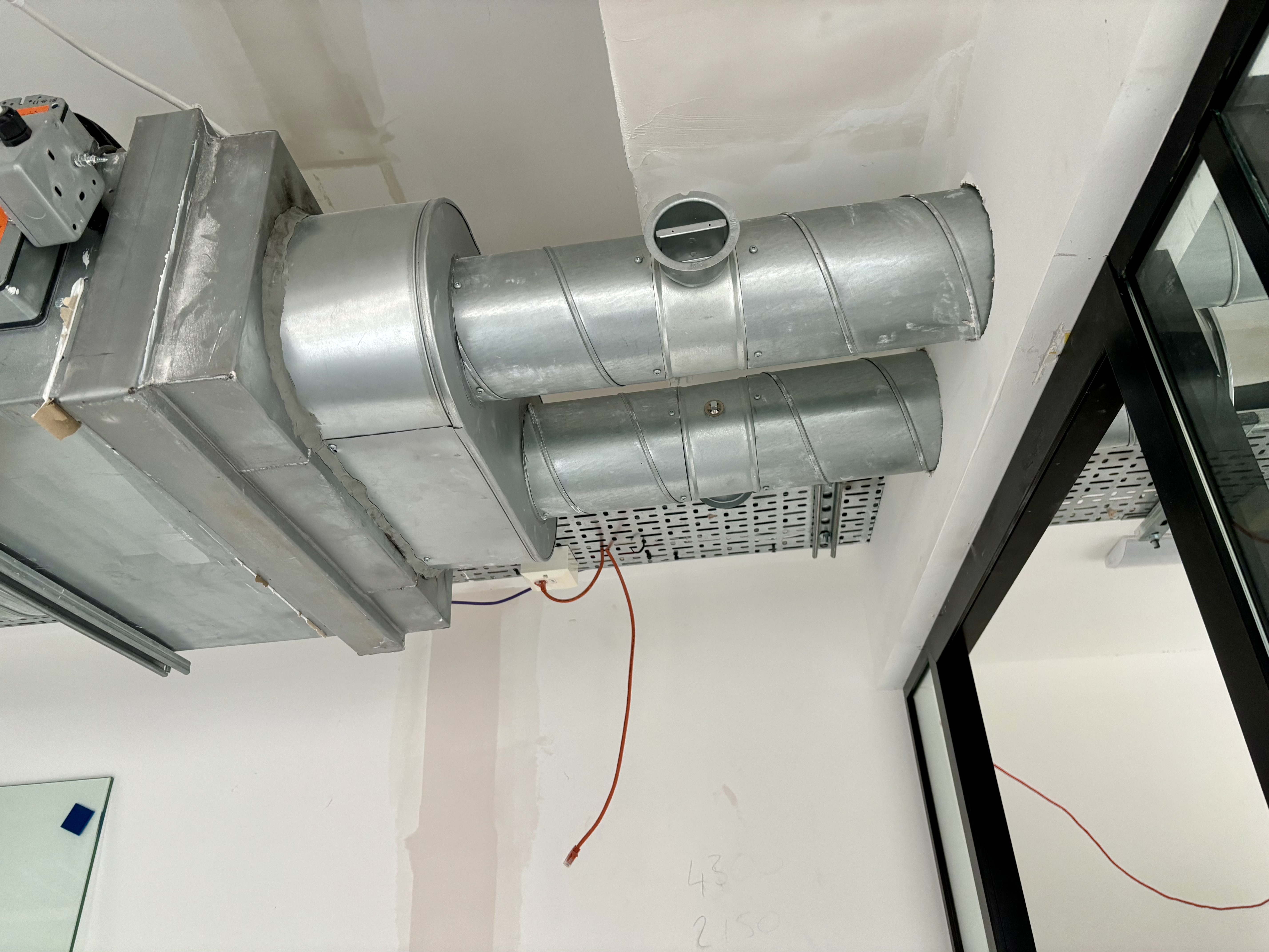 Industrial silver HVAC ducts and a ventilation unit installed on a white unfinished ceiling.